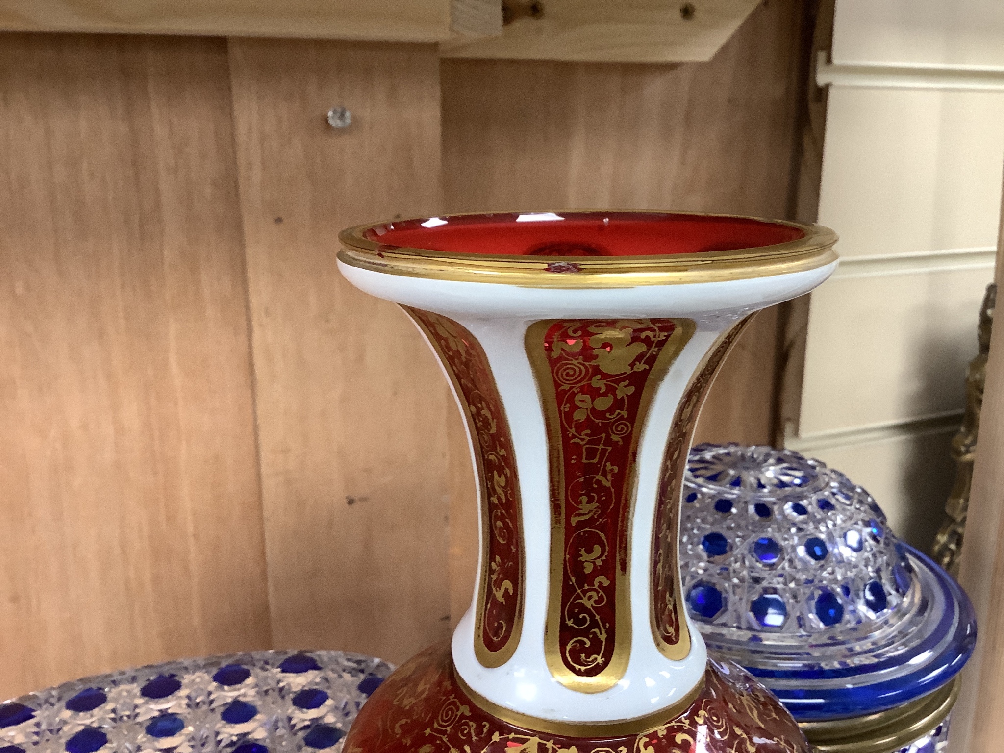 A 19th century Bohemian overlaid glass vase, 25.5cm, a similar gilded and enamelled beaker and two blue flashed hobnail glass biscuit boxes and covers